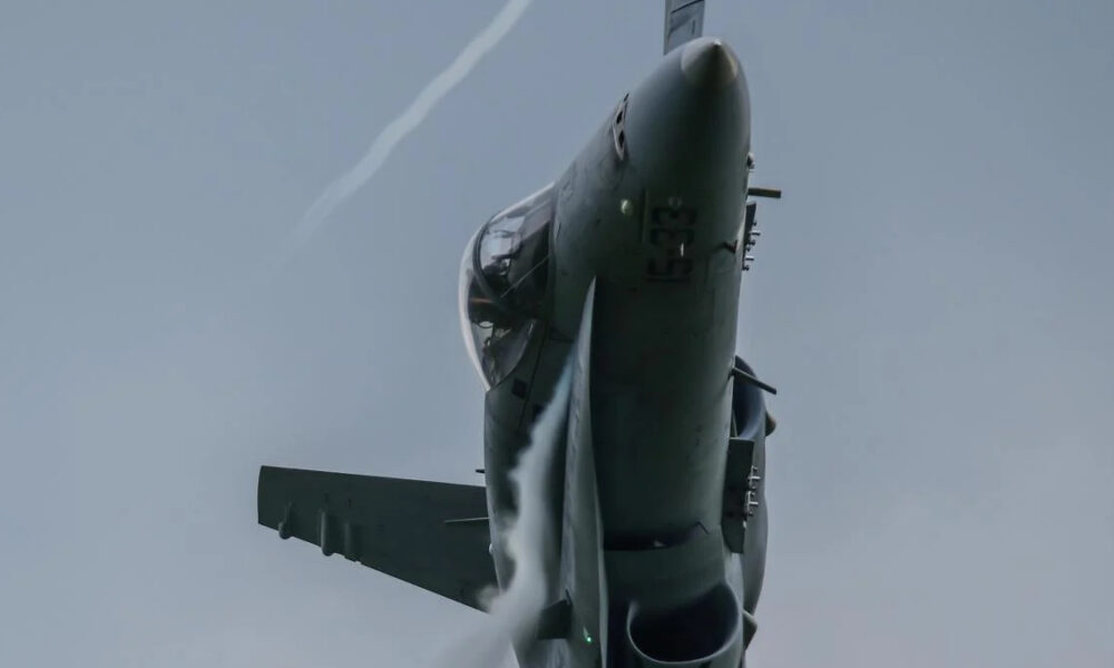 Fighter jet photographed from below during a high- elevator climb against a blue sky, showing the cockpit and forward fuselage.