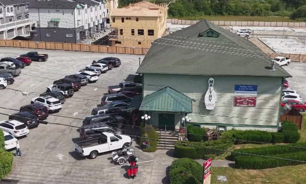Aerial view of a green-roofed restaurant with a circular sign, surrounded by a long line of parked cars in a large lot, and construction in the background.