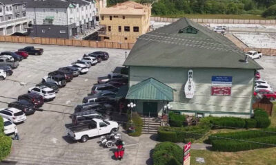 Aerial view of a green-roofed restaurant with a circular sign, surrounded by a long line of parked cars in a large lot, and construction in the background.
