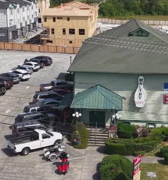 Aerial view of a green-roofed restaurant with a circular sign, surrounded by a long line of parked cars in a large lot, and construction in the background.