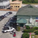 Aerial view of a green-roofed restaurant with a circular sign, surrounded by a long line of parked cars in a large lot, and construction in the background.
