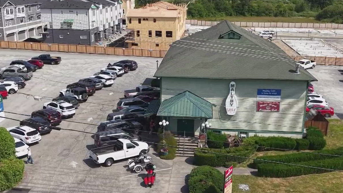 Aerial view of a green-roofed restaurant with a circular sign, surrounded by a long line of parked cars in a large lot, and construction in the background.