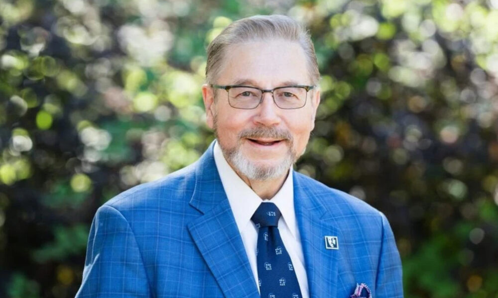 Smiling man with glasses in a blue checkered suit, outdoors.
