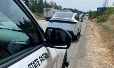 State Patrol car on the shoulder captures traffic ahead; a white car and semi trucks on a rural highway.