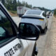 State Patrol car on the shoulder captures traffic ahead; a white car and semi trucks on a rural highway.