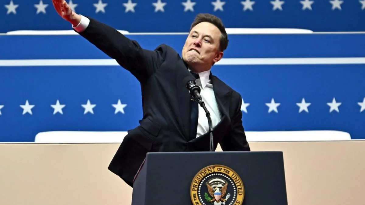 Man in a dark suit at a podium with the presidential seal, raising one arm in front of a blue starry backdrop.