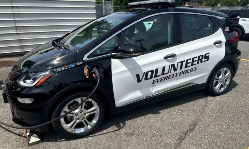 Black-and-white police volunteer car labeled 'Volunteers Everett Police' with a charging cable plugged in.