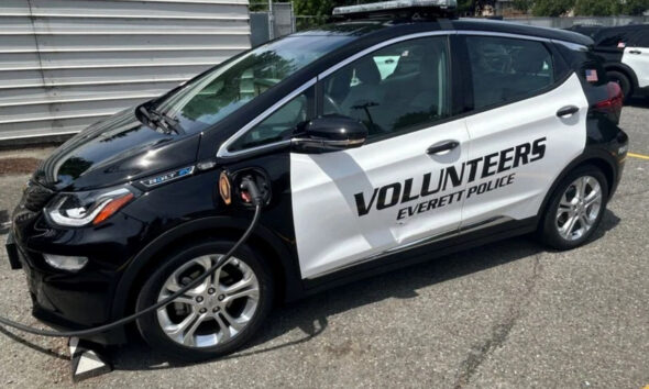 Black-and-white police volunteer car labeled 'Volunteers Everett Police' with a charging cable plugged in.