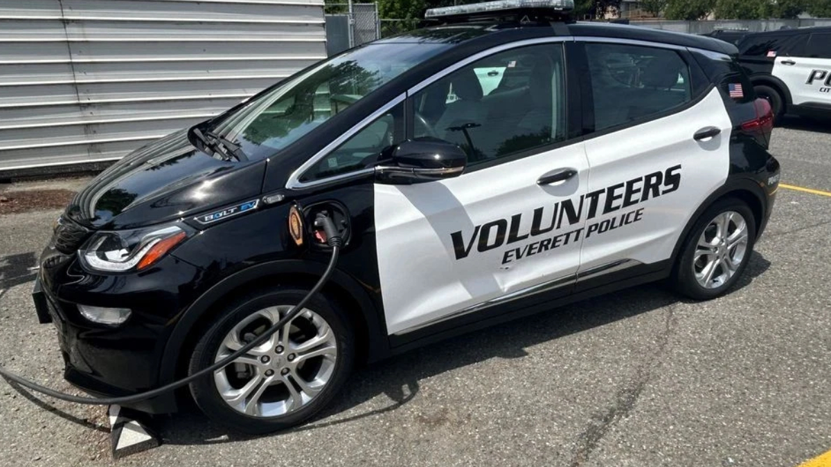Black-and-white police volunteer car labeled 'Volunteers Everett Police' with a charging cable plugged in.