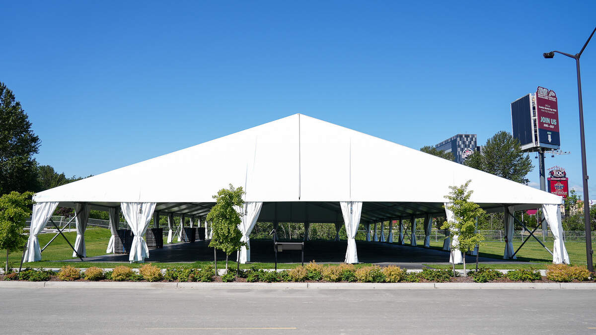 Large white outdoor event tent with open sides and tied-back curtains on a grassy lot, under a clear blue sky.