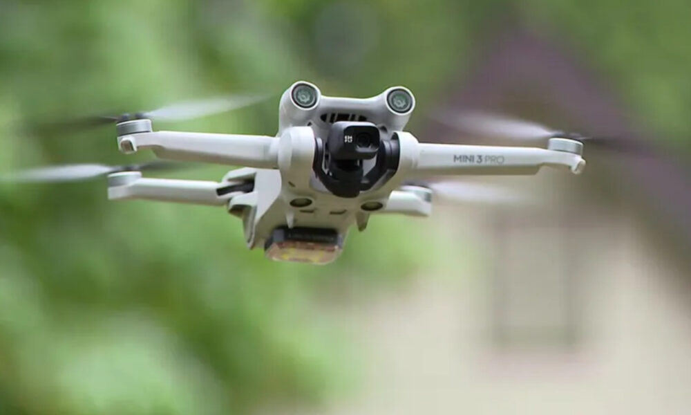 Front view of a white DJI Mini 3 Pro quadcopter in flight with a green outdoor background.