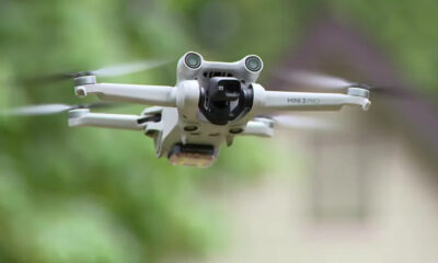 Front view of a white DJI Mini 3 Pro quadcopter in flight with a green outdoor background.