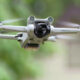 Front view of a white DJI Mini 3 Pro quadcopter in flight with a green outdoor background.