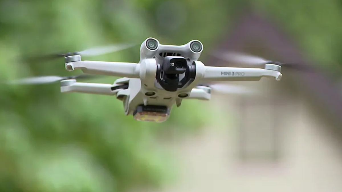 Front view of a white DJI Mini 3 Pro quadcopter in flight with a green outdoor background.