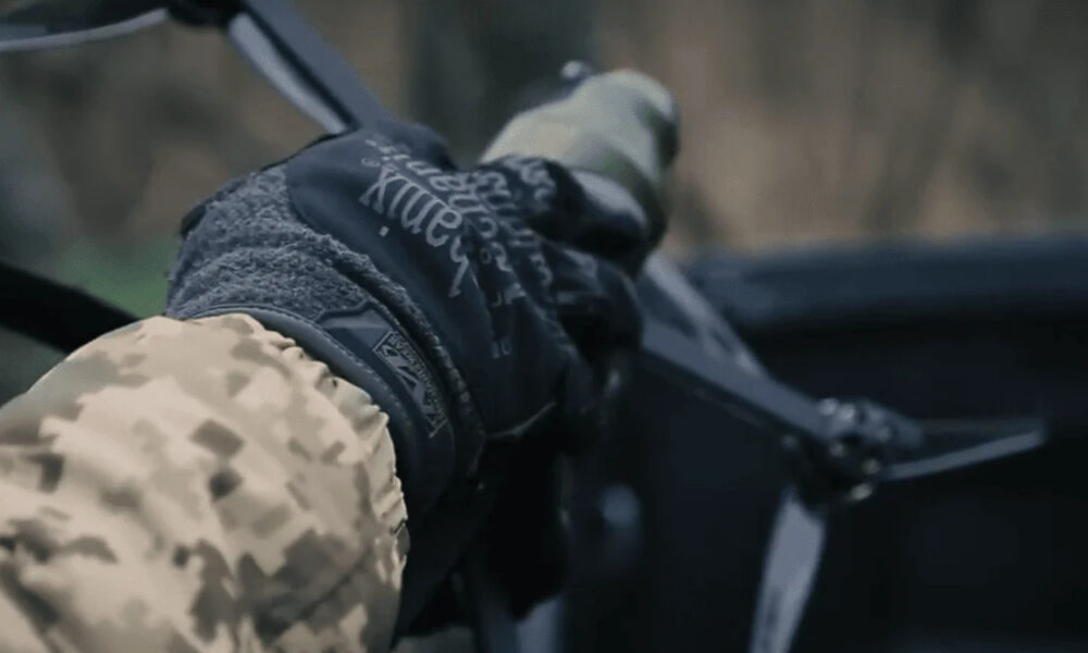 Close-up of a camo-sleeved arm and black glove gripping a firearm inside a car or vehicle cockpit.