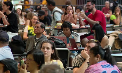 Crowded indoor dining area with people seated at tables, eating and using laptops.