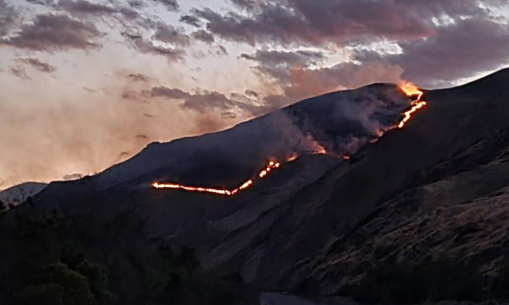Volcano erupting at dusk with a glowing lava flow tracing a ridge down the slope.