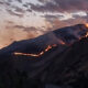 Volcano erupting at dusk with a glowing lava flow tracing a ridge down the slope.