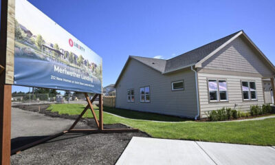 New housing development sign for Meriwether Landing beside a beige ranch-style house under construction. The sign shows a blue sky and green landscaping image.