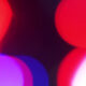 Abstract background of red, pink, and purple bokeh lights on a dark backdrop.