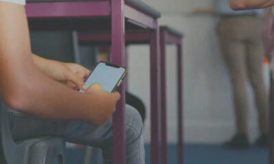 Person seated, using a smartphone; purple chair frames are visible in the background (indoor setting).