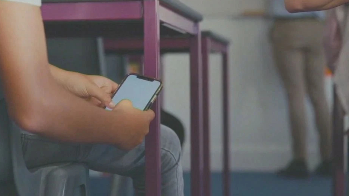Person seated, using a smartphone; purple chair frames are visible in the background (indoor setting).