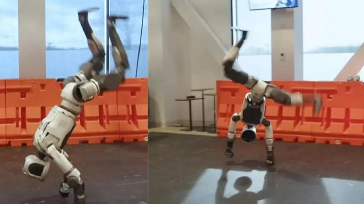 Two humanoid robots performing backflips on a lab floor with orange safety barriers in the background, mid-air with arms raised.