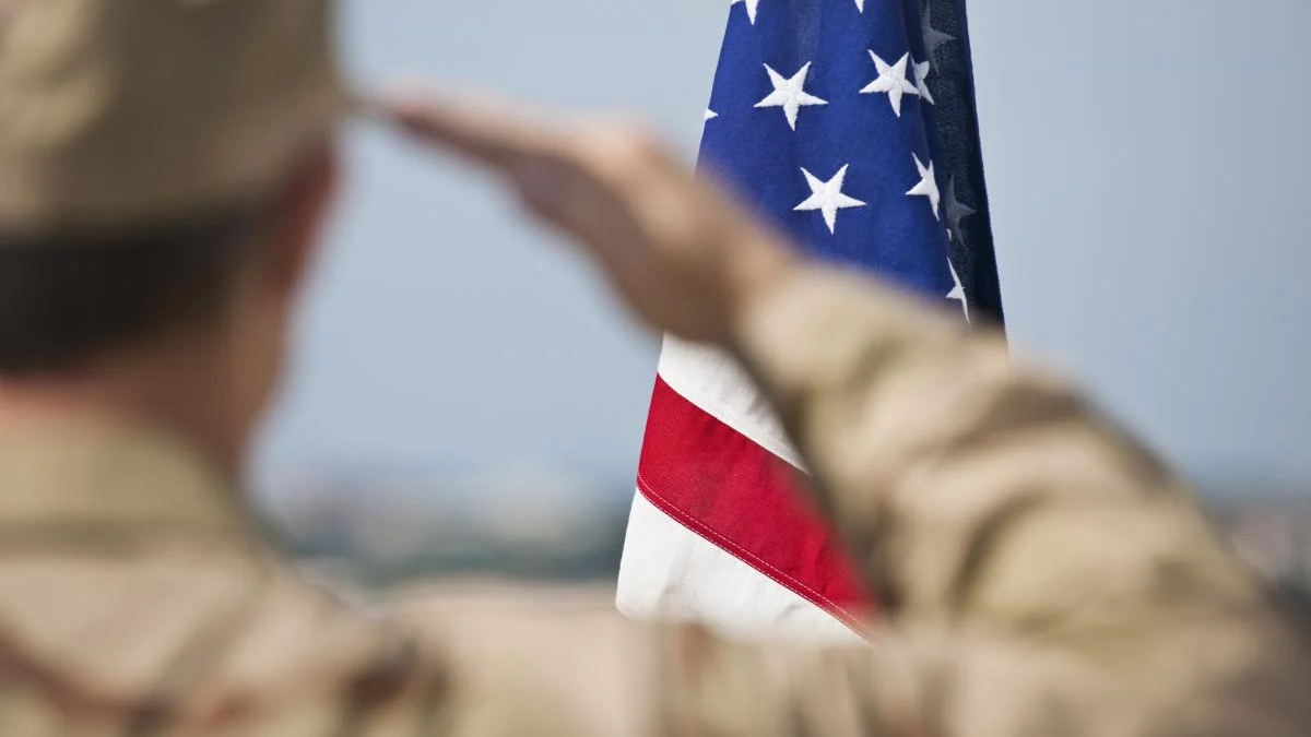 A service member in uniform saluting with the American flag in the foreground.
