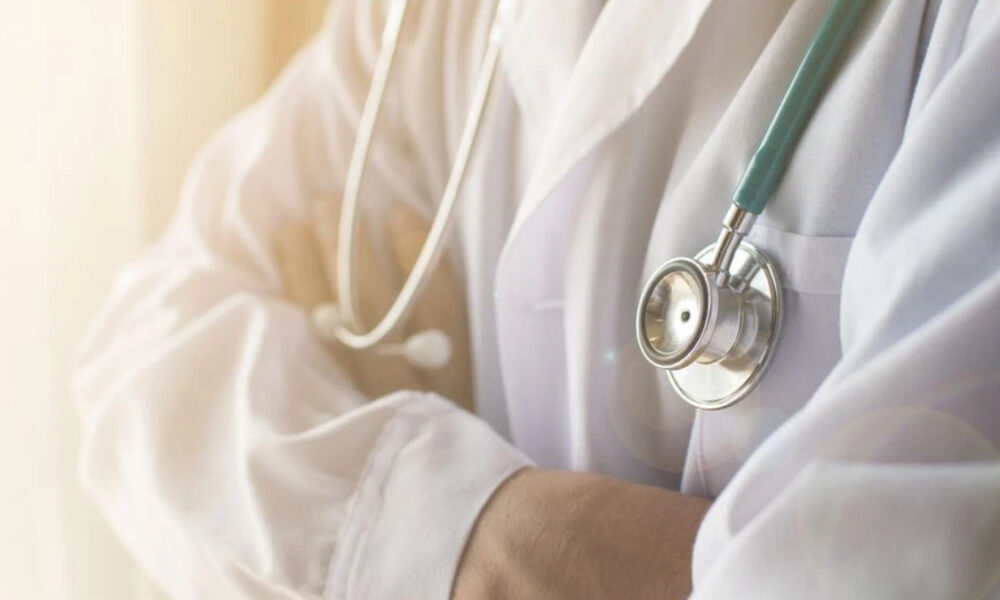 Medical professional in a white coat with a stethoscope draped around the neck, ready to examine a patient.