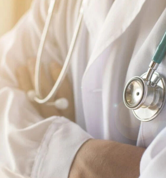 Medical professional in a white coat with a stethoscope draped around the neck, ready to examine a patient.