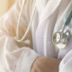 Medical professional in a white coat with a stethoscope draped around the neck, ready to examine a patient.