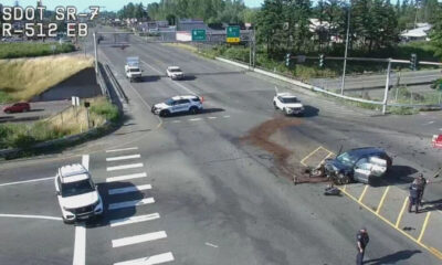 Overhead view of a four-way intersection crash with a damaged car on the right, debris on the road, and police vehicles blocking lanes.