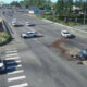 Overhead view of a four-way intersection crash with a damaged car on the right, debris on the road, and police vehicles blocking lanes.
