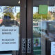 Glass storefront door with multiple signs; main message reads 'DOOR OUT OF SERVICE. PLEASE USE OTHER DOOR.' and 'Driving School' window text visible.