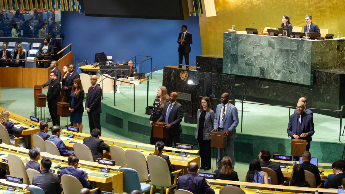 Delegates stand at podiums in the United Nations General Assembly chamber during a session.