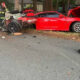 Red sports car smashed into a tree with extensive front-end damage; firefighters in turnout gear survey the crash scene.