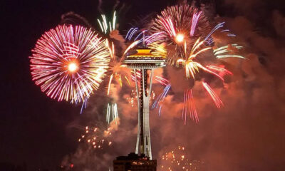 Fireworks explode around Seattle's Space Needle at night, colorful bursts lighting the sky above the city.