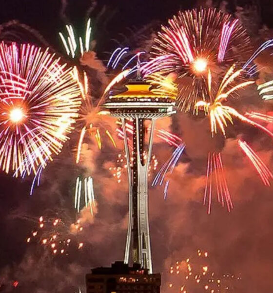 Fireworks explode around Seattle's Space Needle at night, colorful bursts lighting the sky above the city.