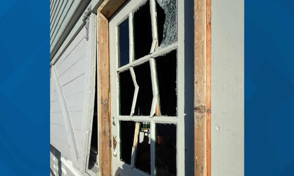 Broken window in a wooden frame of a weathered house, glass shattered and openings exposed inside the room
