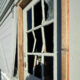 Broken window in a wooden frame of a weathered house, glass shattered and openings exposed inside the room
