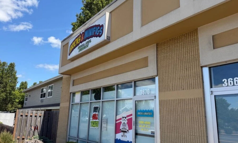Storefront of a shop with large glass windows and a colorful sign reading '... & Minifigs' under a clear blue sky; street numbers 3670 and 3660 visible.