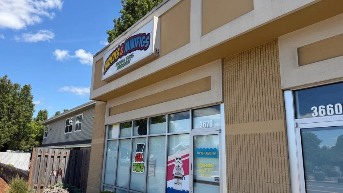 Storefront of a shop with large glass windows and a colorful sign reading '... & Minifigs' under a clear blue sky; street numbers 3670 and 3660 visible.