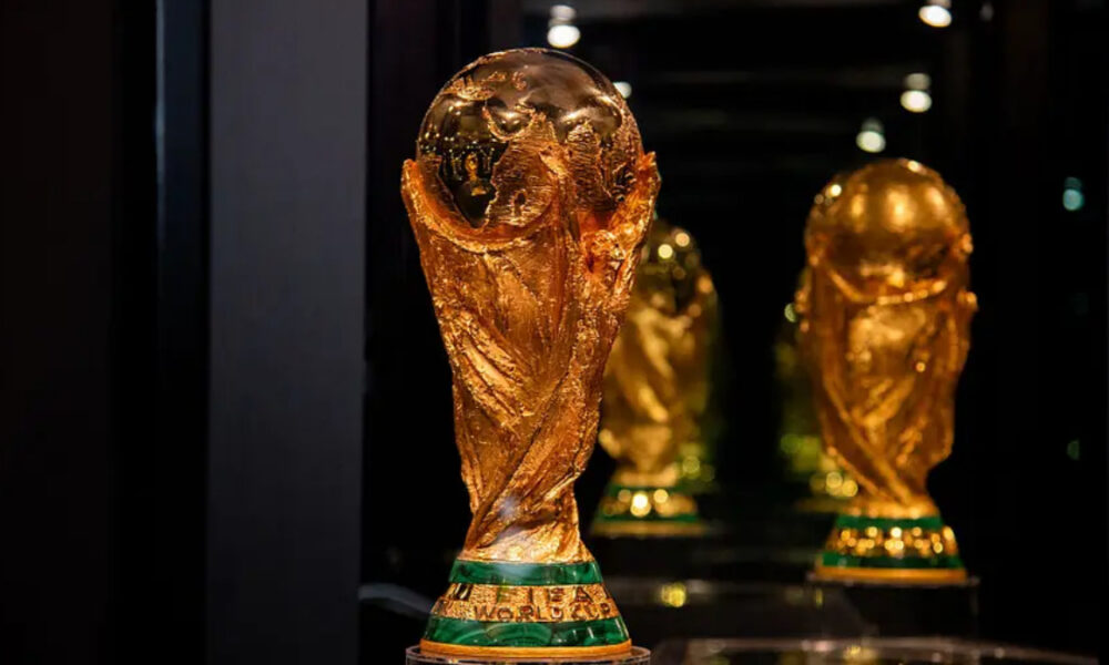 Close-up of the FIFA World Cup trophy on a pedestal in a dim display case.