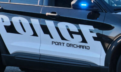 Police car side panel with a blue flashing emergency light and the word POLICE, PORT ORCHARD visible on the door.