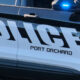 Police car side panel with a blue flashing emergency light and the word POLICE, PORT ORCHARD visible on the door.