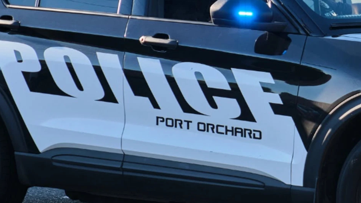 Police car side panel with a blue flashing emergency light and the word POLICE, PORT ORCHARD visible on the door.