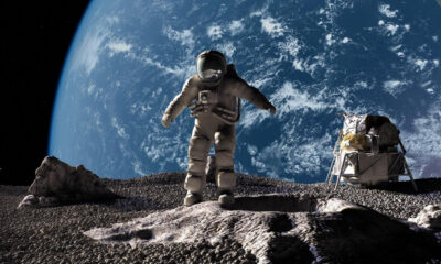 Astronaut in a spacesuit stands on the Moon's rocky surface with Earth visible in the background and a lunar lander nearby.
