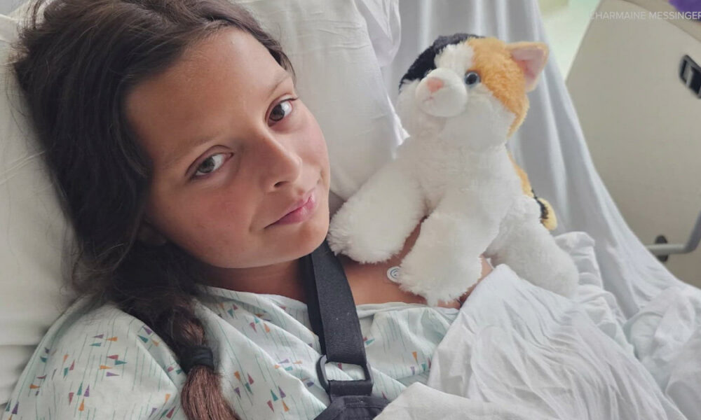 Young girl lying in a hospital bed, holding a plush calico cat for comfort.