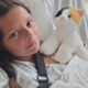 Young girl lying in a hospital bed, holding a plush calico cat for comfort.