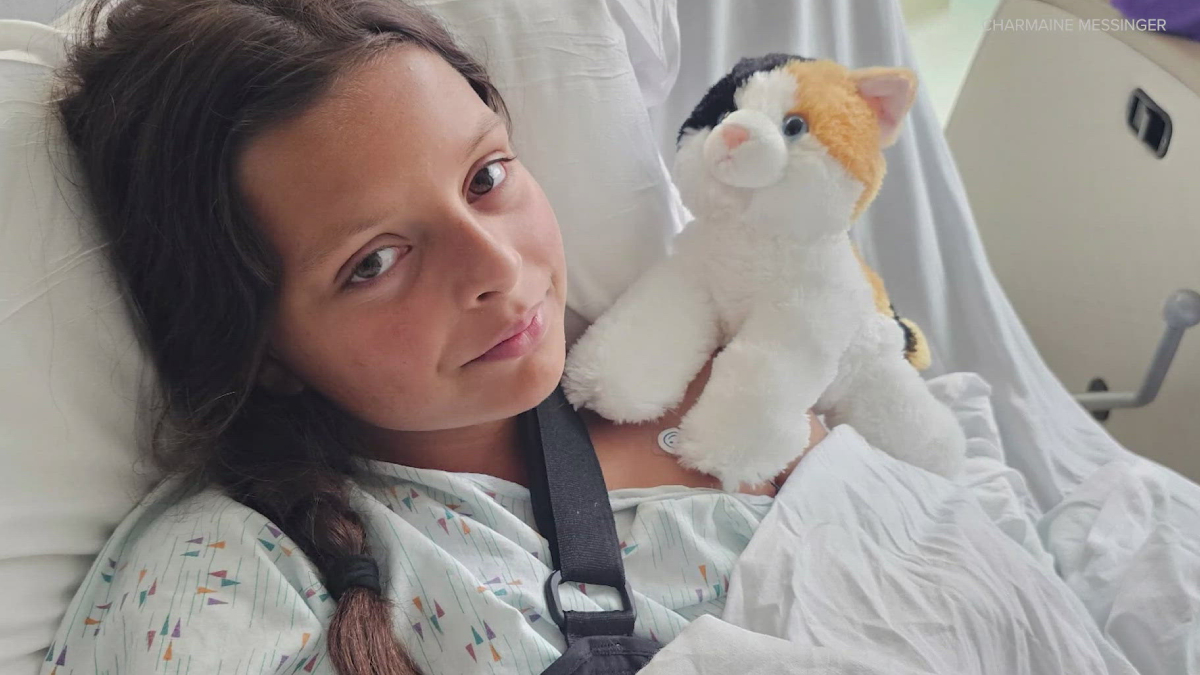 Young girl lying in a hospital bed, holding a plush calico cat for comfort.